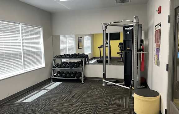 A gym room with a weight rack, a bench, and a window.