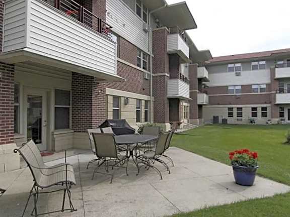 A patio with a table and chairs is in front of a brick building.