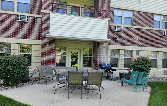 A patio with a table and chairs is in front of a brick building.