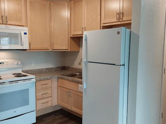 A kitchen with a white refrigerator, white stove, and wooden cabinets.
