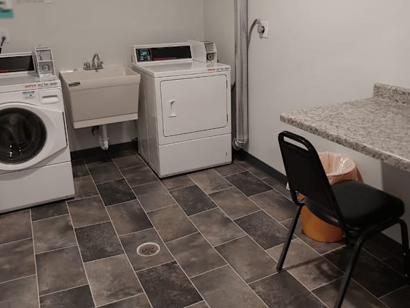 A laundry room with a washer and dryer, a chair, and a counter.