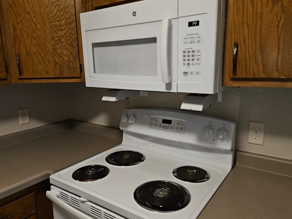 A white microwave is mounted above a white stove in a kitchen.