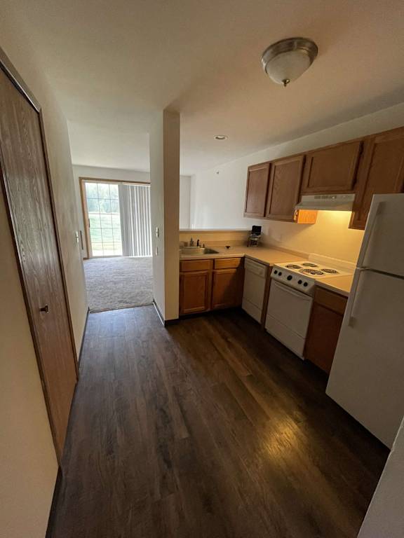 an empty kitchen with wood flooring and white appliances