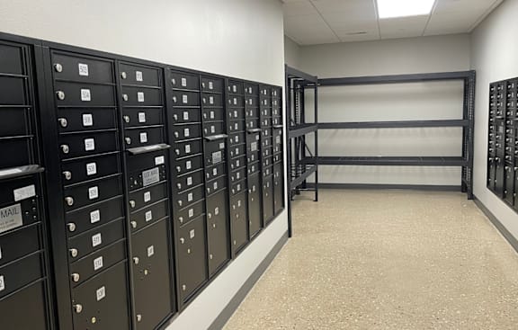 A room with a wall of mailboxes and a shelf.