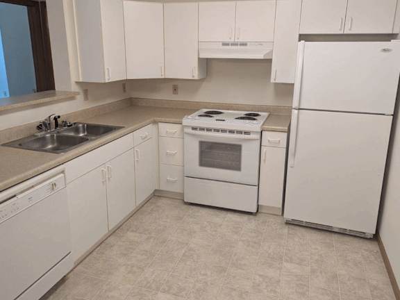 A white kitchen with a stove, sink, and refrigerator.