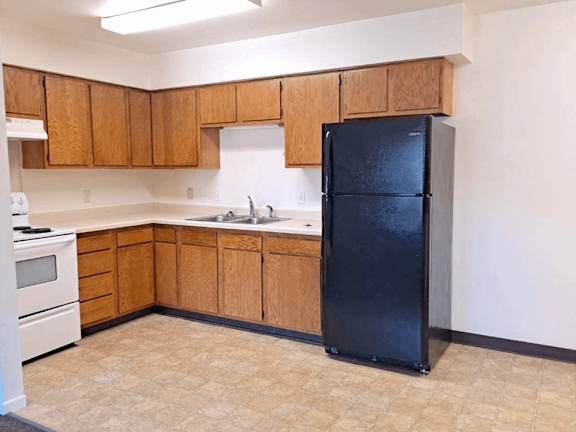 A kitchen with wooden cabinets and a black refrigerator.