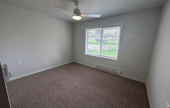 A room with a ceiling fan and a window overlooking a parking lot.