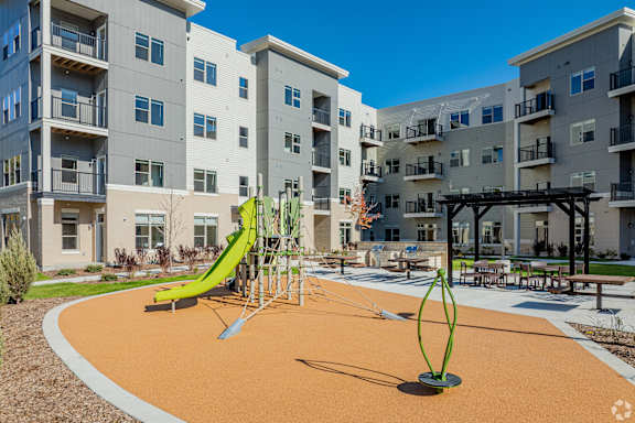 A playground with a green slide and a yellow swing set in front of apartment buildings.
