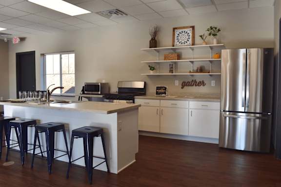 A kitchen with white cabinets and a refrigerator with a sign that says "gather" on it.
