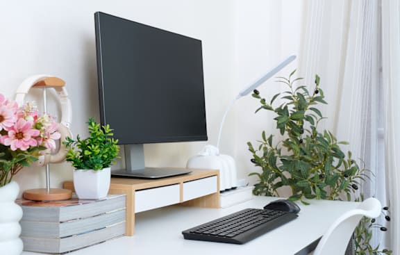 A black monitor sits on a desk with a keyboard and a plant.