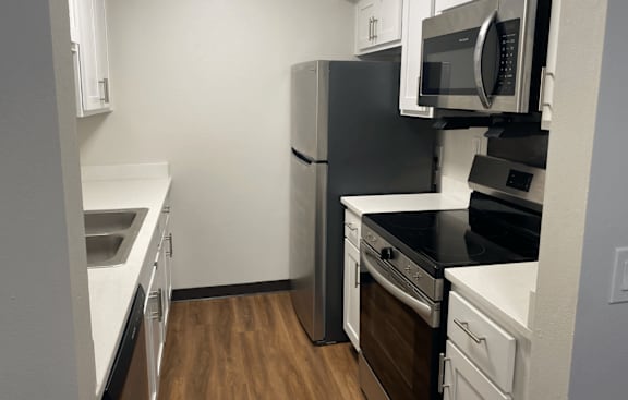 A black refrigerator and microwave in a kitchen with white cabinets.