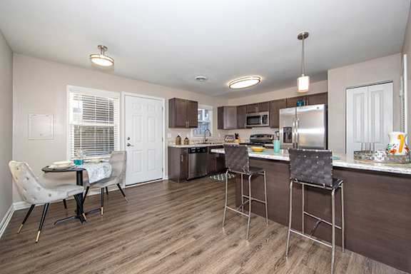 A kitchen with a table and chairs in the foreground and a refrigerator, microwave, and oven in the background.