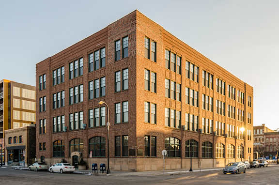 A large red brick building with many windows and cars parked in front.
