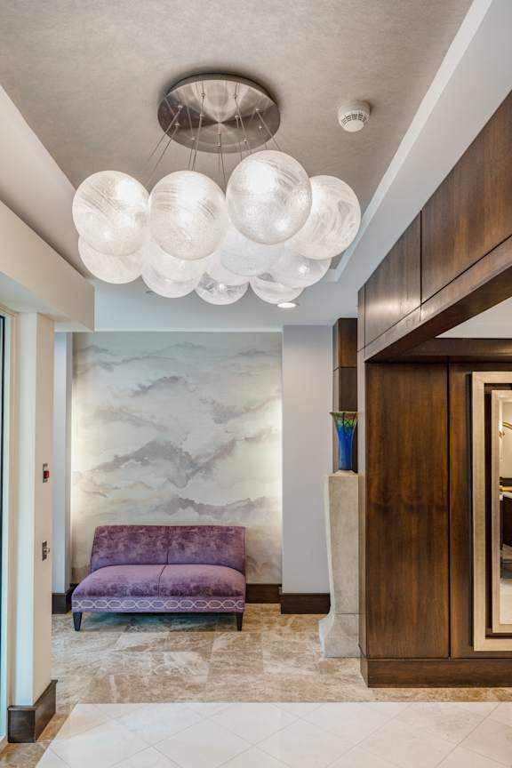 A purple sofa sits in front of a marble wall.