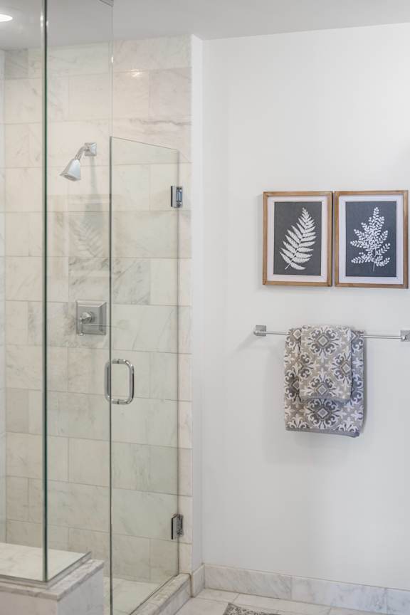 A bathroom with a glass shower door and a towel rack with two towels.