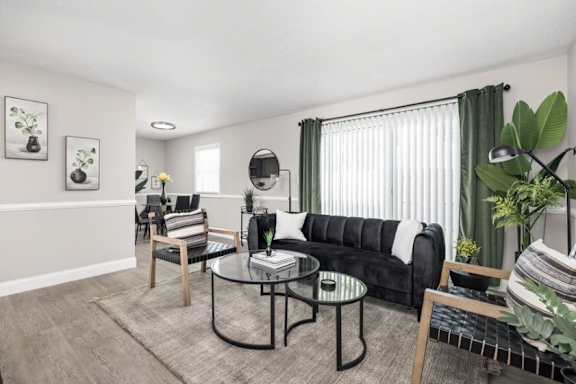 A living room with a black couch, a glass table, and a grey rug.