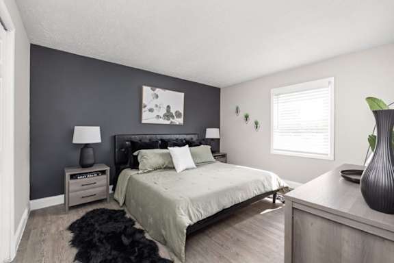 A bedroom with a bed, nightstand, lamp, and a plant.