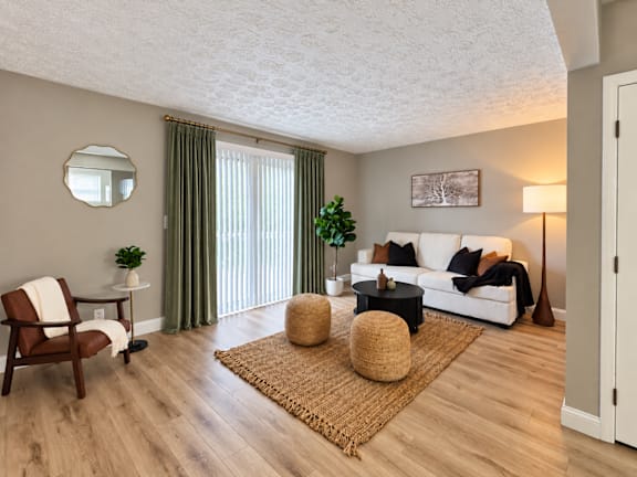 A living room with a white couch, a wooden chair, and a round mirror on the wall.