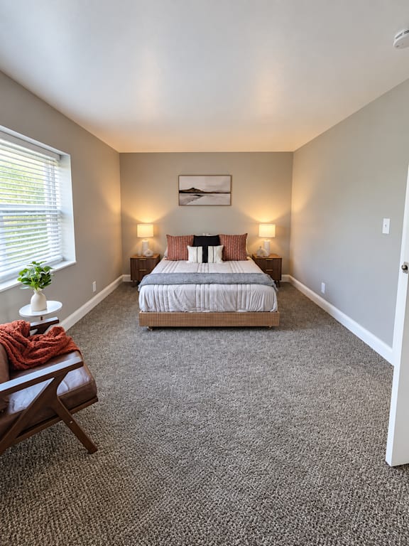 A bedroom with a bed, two lamps, a chair, and a painting on the wall.
