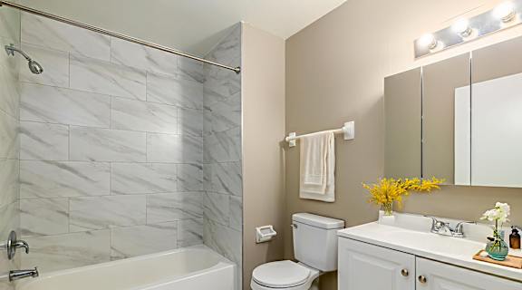 A bathroom with a marble tile shower, white bathtub, toilet, and sink.