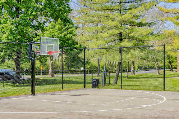 A basketball court surrounded by a fence with a basketball hoop on the left side.
