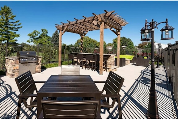 A wooden table and chairs are set up under a pergola on a patio.