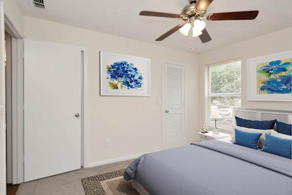 A bedroom with a bed, pillows, a ceiling fan, and two framed pictures on the wall.