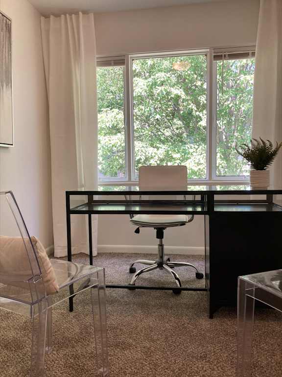 A black desk with a glass top and a white chair in front of a window with trees visible outside.