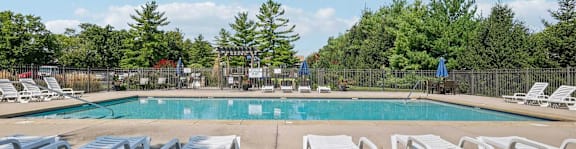 A pool surrounded by trees and chairs.