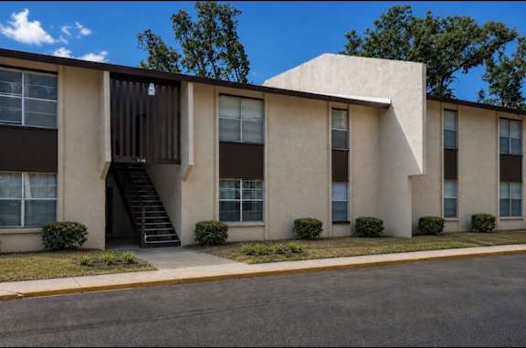 A building with a brown and beige exterior and a black staircase leading to the entrance.