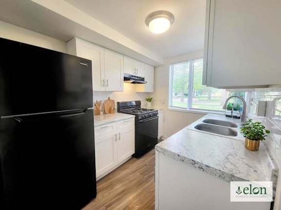 A kitchen with a black fridge, white cabinets, and a marble countertop.