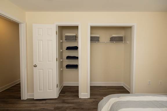 A bedroom with a white bed and a white closet with shelves.