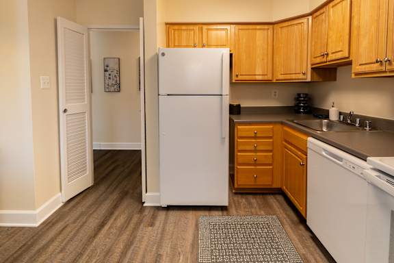 A white refrigerator stands in a kitchen with wooden cabinets and a white stove.
