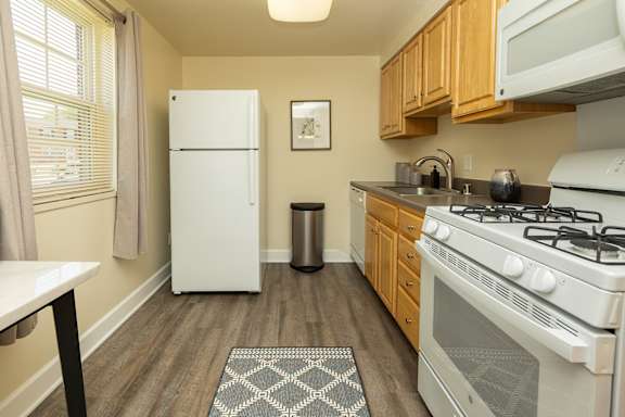 A kitchen with a white fridge, a white stove, and wooden cabinets. at Colony Hill Apartments &amp; Townhomes, Baltimore, MD