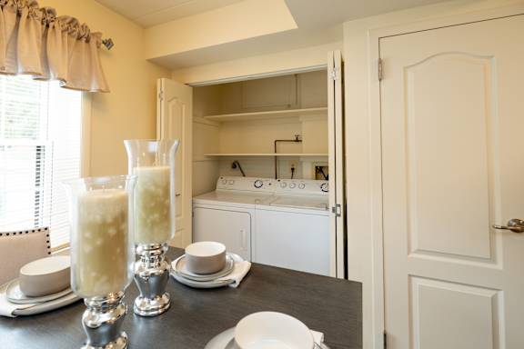 A kitchen with a table set for two and a window with curtains  at Ivy Hall Apartments*, Maryland, 21204