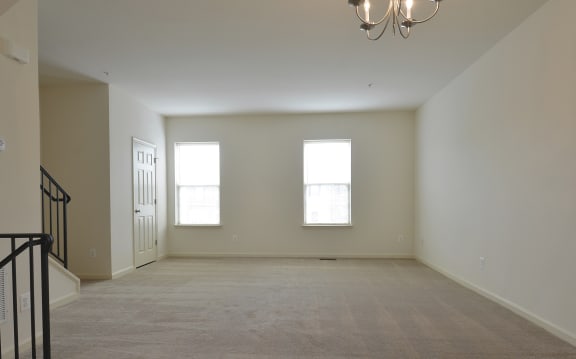 Empty living room with three windows and a chandelier at The Pointe at Manorgreen Townhomes, Baltimore, MD