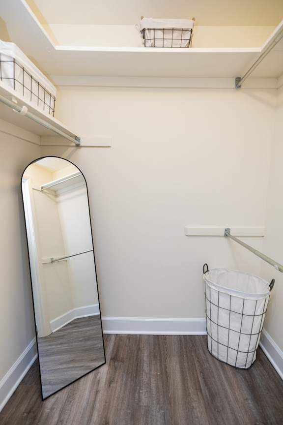 A small white laundry basket sits on a wooden floor in a small room.
