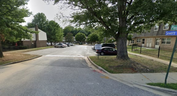 Parking lot in front of a building with a tree in the middle of the parking lot at The Orchards at Severn Townhomes*, Severn, MD 21144