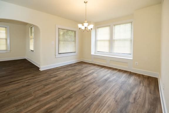 an empty living room with a chandelier and three windows at Ivy Hall Apartments*, Maryland, 21204