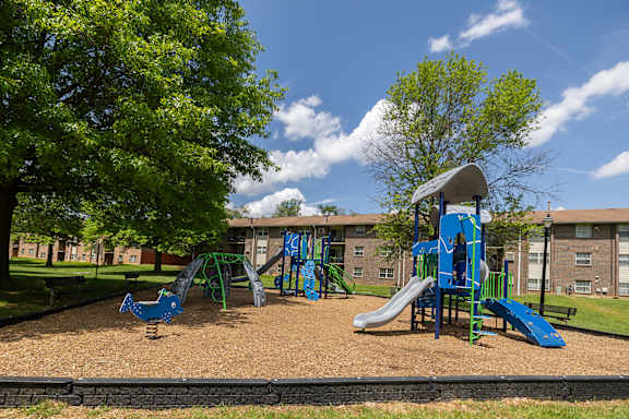 A playground with a blue slide and a green tree.at Deer Park Apartments, Randallstown