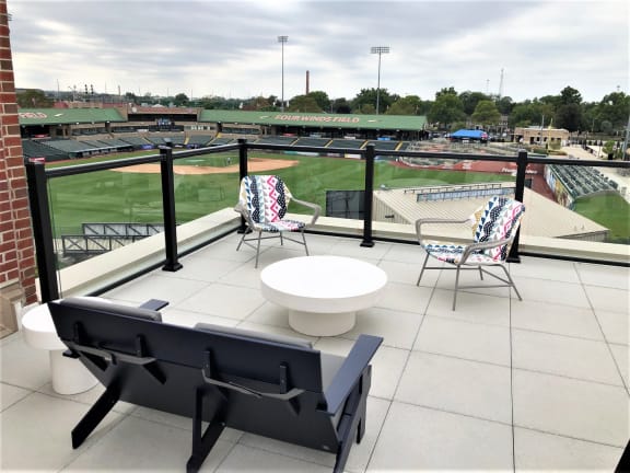 a rooftop terrace with chairs and tables overlooking a baseball field