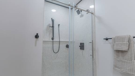 A white bathroom with a glass shower door and a towel hanging on the towel rack.