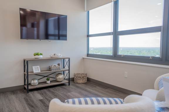 A living room with a flat screen TV mounted on the wall and a window with a view of the city.