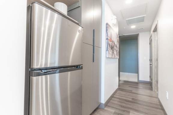 A stainless steel refrigerator in a hallway with wood flooring.