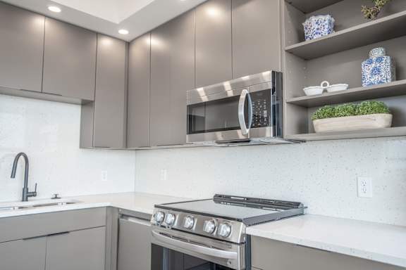 A modern kitchen with a stove, microwave, and shelves with dishes.