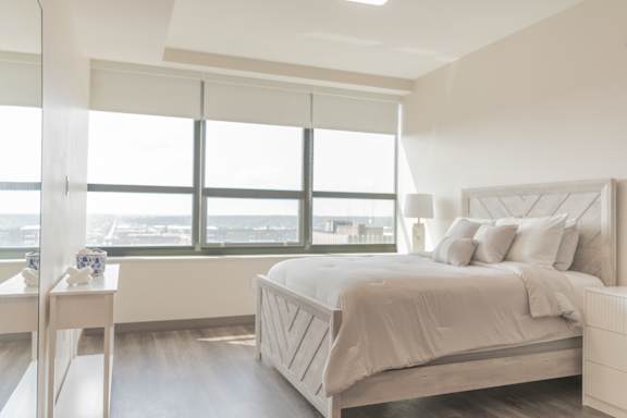A white bedroom with a large bed and a view of the city.
