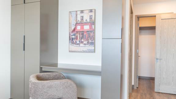 A chair sits in a corner of a room with a picture of a red building on the wall.