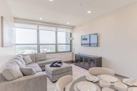 A modern living room with a grey sofa, a grey coffee table, a white chair, and a flat screen TV mounted on the wall.