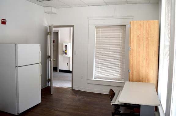 A white refrigerator is in a room with a white door and a brown table.