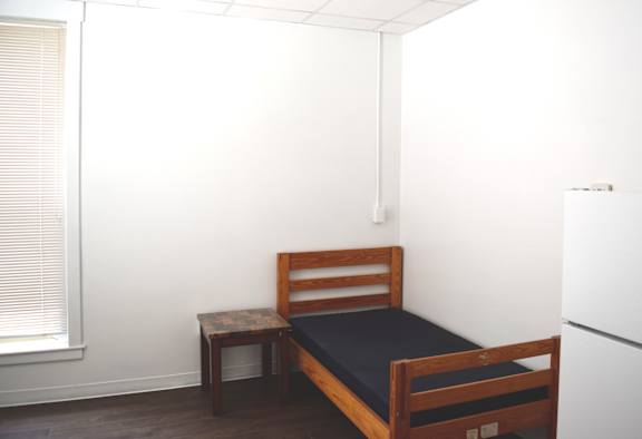 A bedroom with a bed, a small table, and a window with blinds.